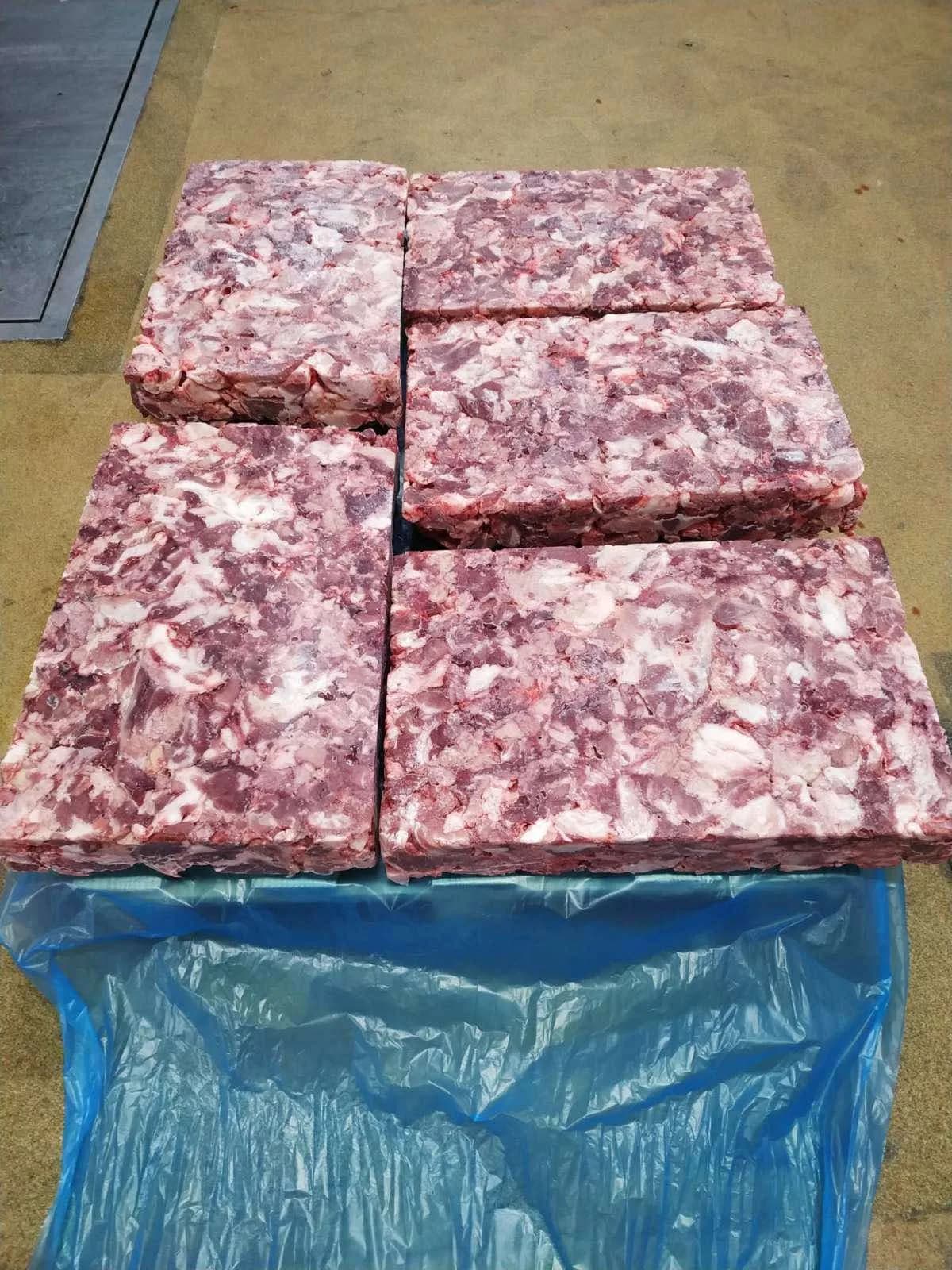 Frozen blocks of pork trimmings stacked on a blue-lined pallet, the cut faces showing the lean-to-fat mix.