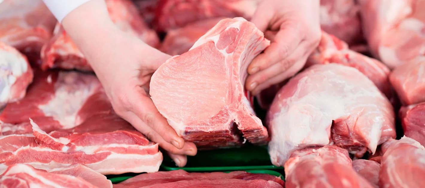 Hands lifting a bone-in pork chop from a tray of freshly cut pieces during selection.