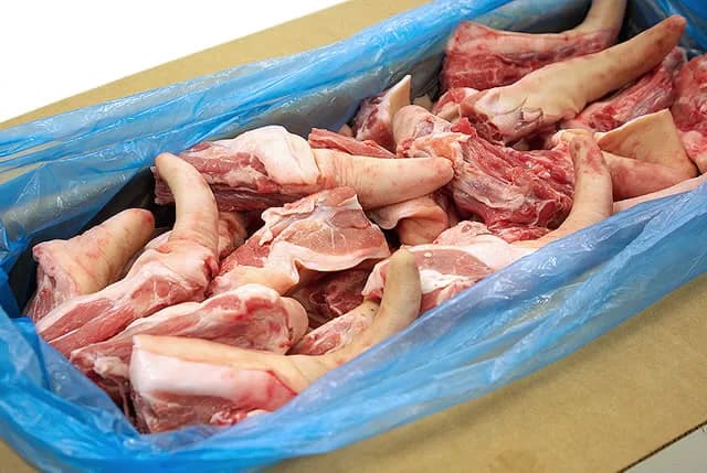 Long pork tails packed in a blue polythene liner inside a cardboard carton.
