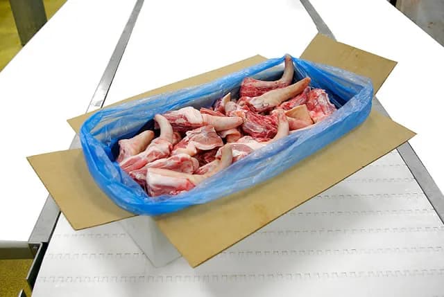 Lined carton of long pork tails on the packing line, flaps open before closing.